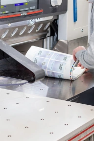 Ein Stapel bedruckter Bogen für die Stickerpacks geht in den Zuschnitt